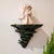 Djamor Fungus Wall Shelf mounted in a living room with decorative items. Sparkling dark green color.